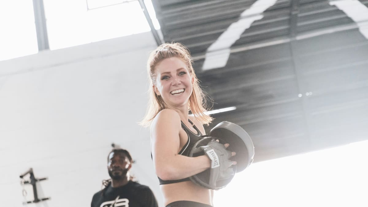 Personal trainer sorri segurando uma manopla de foco em uma academia clara